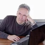 Mann sitzt genervt vor langsamen Win 7-Computer.