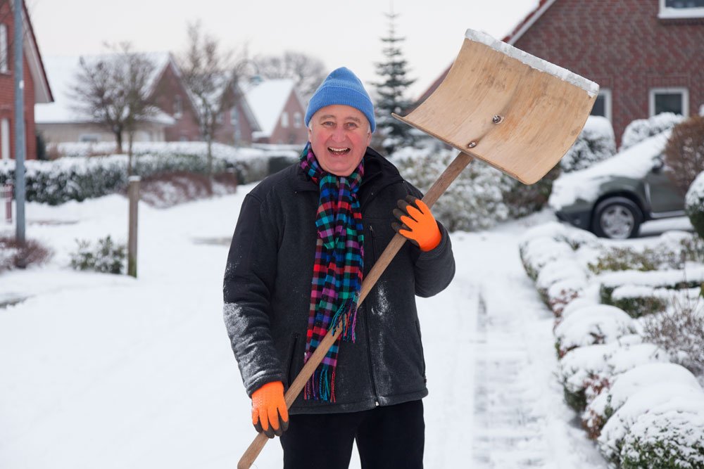 Mann räumt Schnee mit Schneeschieber.