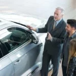 Autohändler zeigt Pärchen einen Gebrauchtwagen.