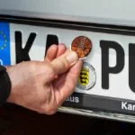 HU-Plakette wird ans Auto geklebt.