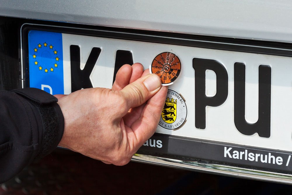 HU-Plakette wird ans Auto geklebt.