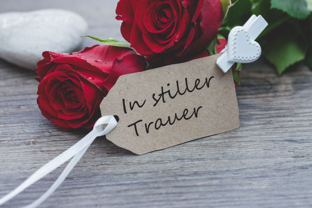 Trauerkarte "In stiller Trauer" vor roten Rosen.